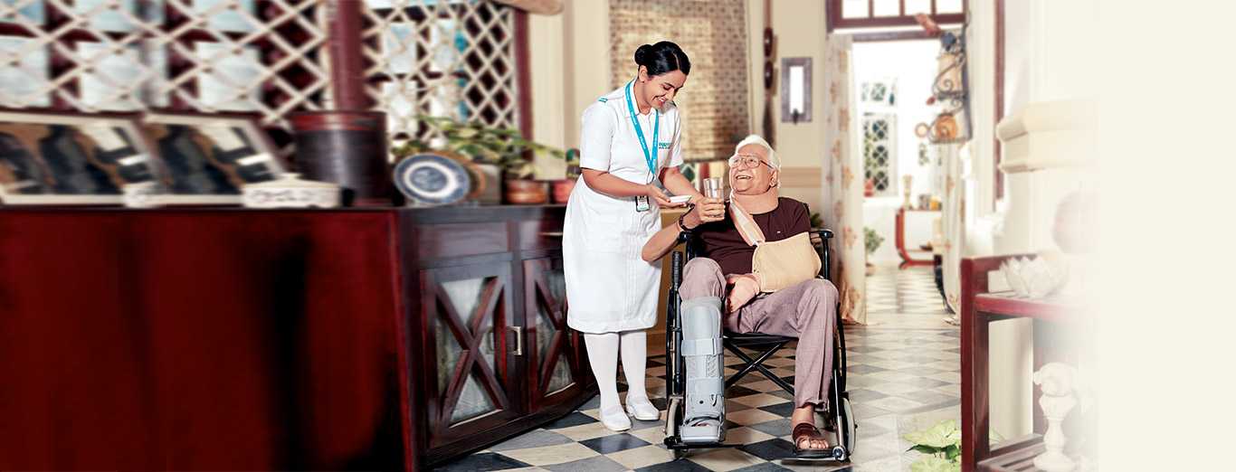 A nurse hands a glass of water to an elderly man in a wheelchair at his home